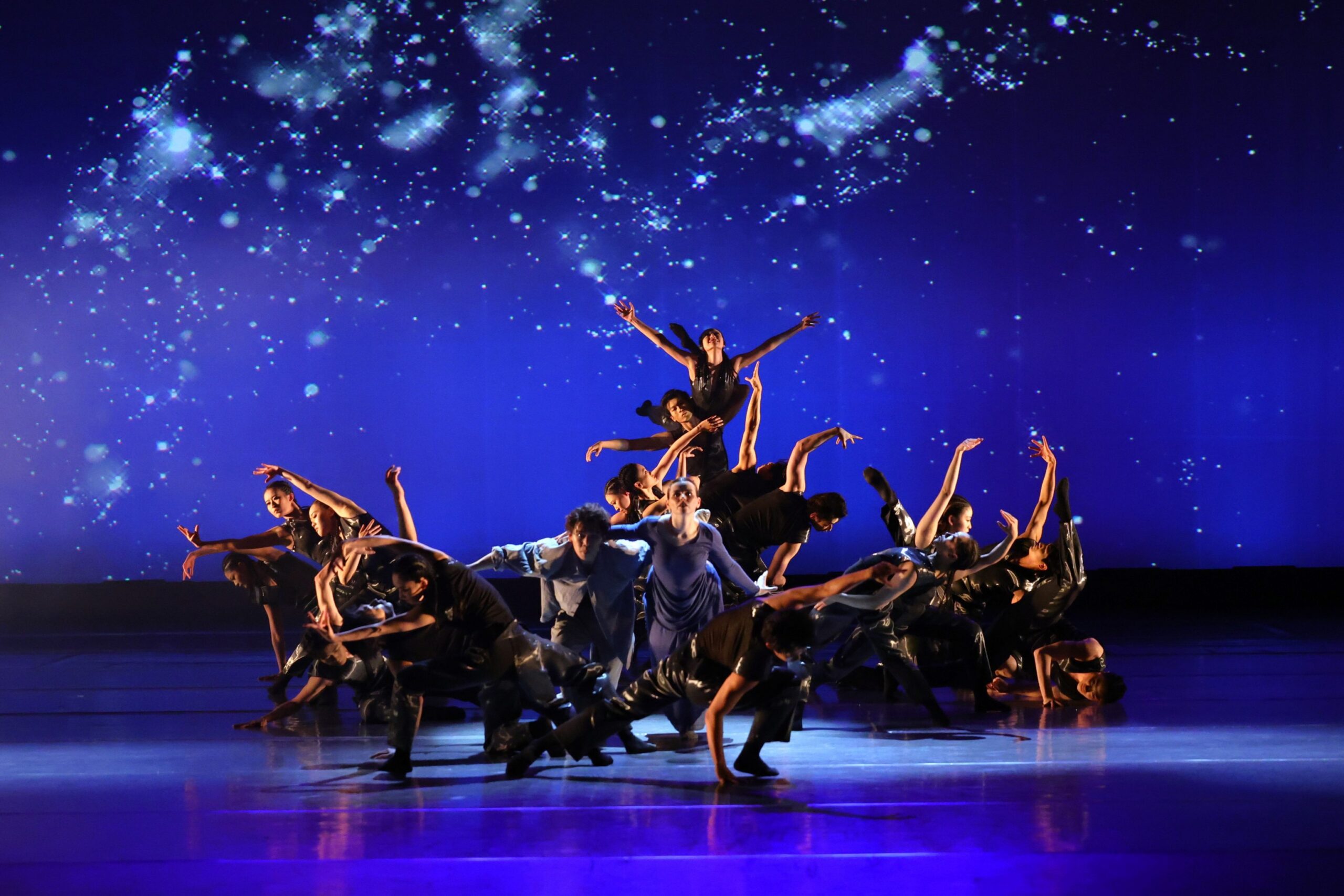 A group of dancers dressed in black/dark blue costumes performing on stage.