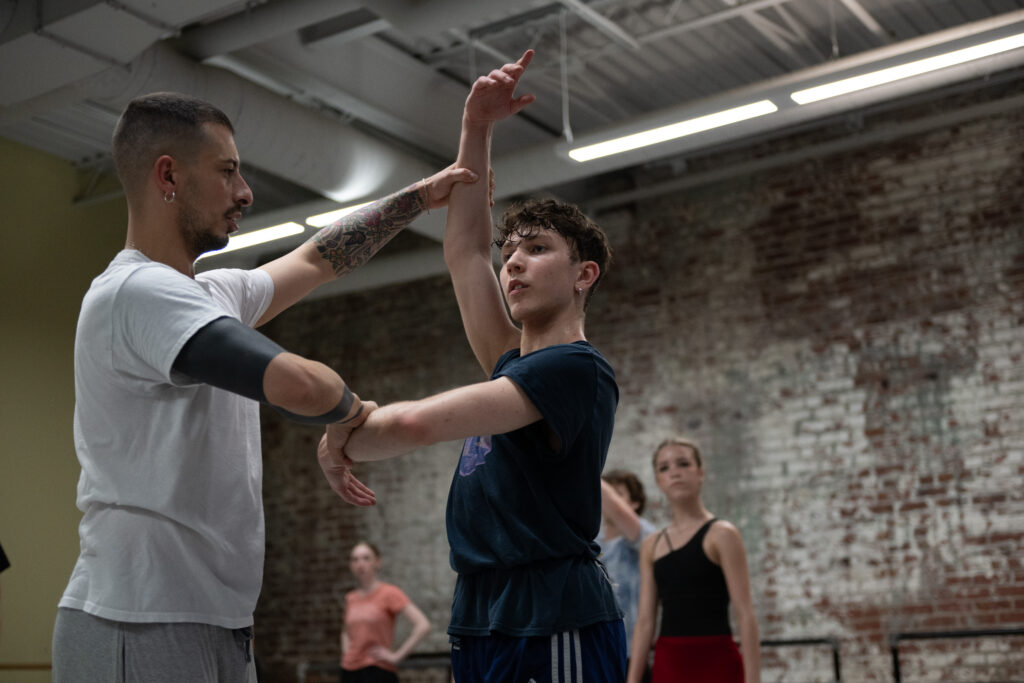 A dance instructor positioning a students arms in the center.