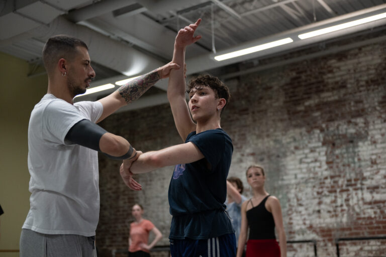 A dance instructor positioning a students arms in the center.