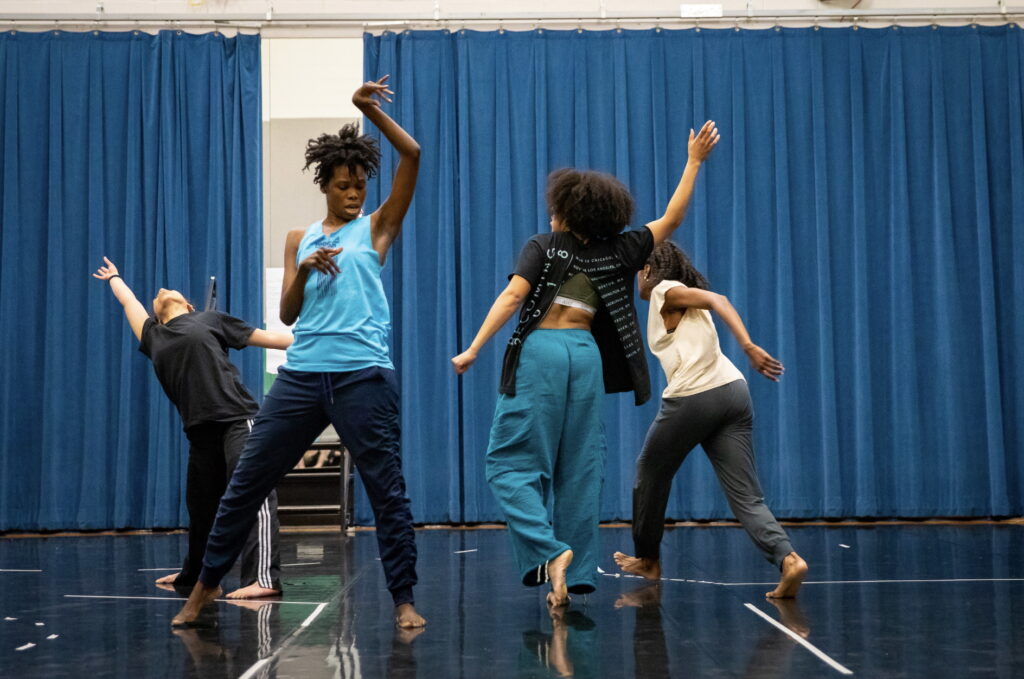 Chanon Judson teaching in a blue top and black pants with students dancing around her.