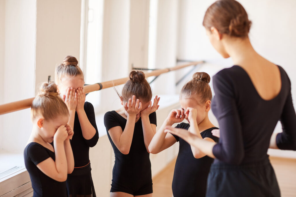 Group of little girls crying during ballet practice in studio with teacher overlooking.