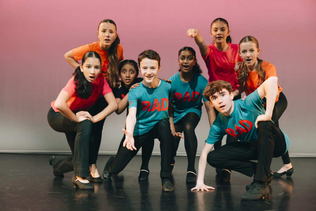 Young performers in blue and red tshirts with RAD written on them singing on stage.