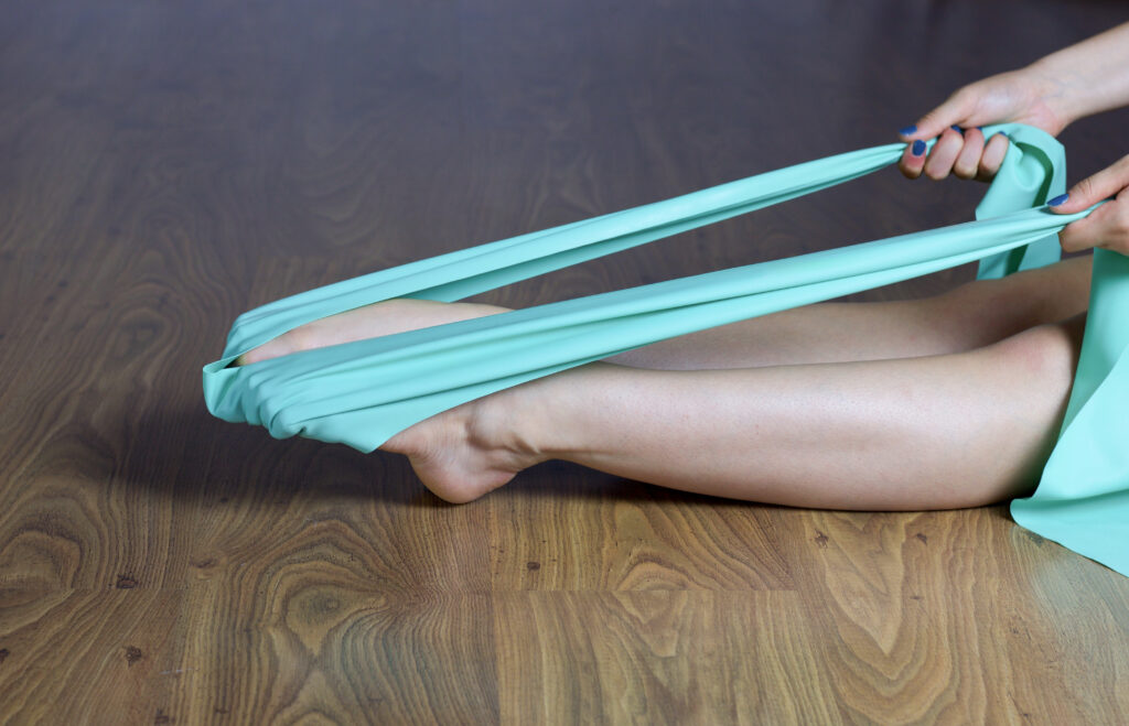 person doing exercices for feet strengtening with elastic band sitting on wooden floor