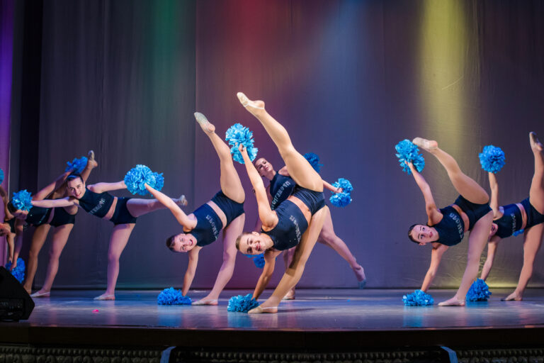 Young cheerleaders perform on stage holding pom poms.
