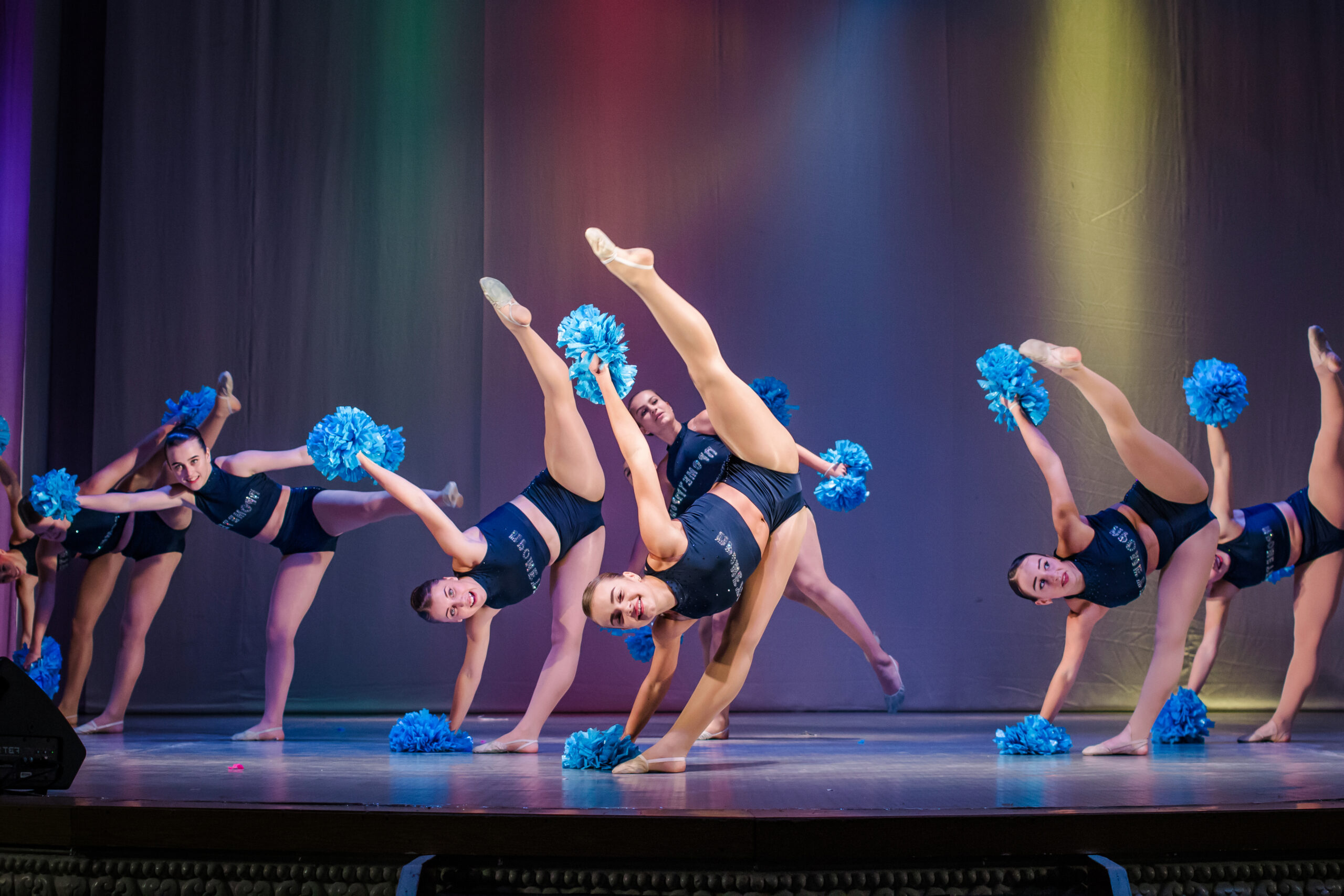 Young cheerleaders perform on stage holding pom poms.