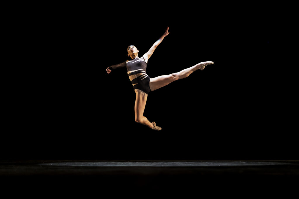 Girl performing contemporary dance on dark stage.