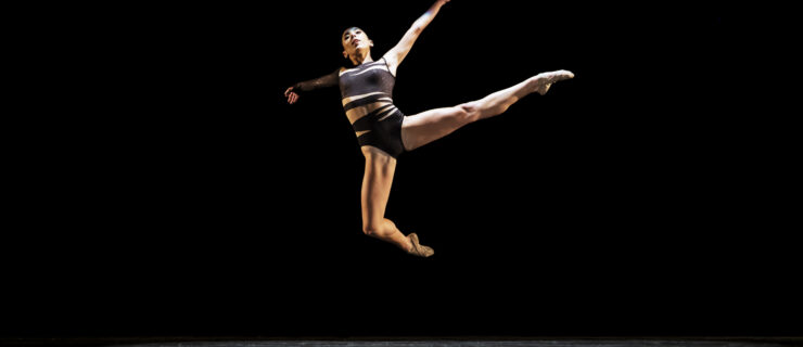 Girl performing contemporary dance on dark stage.