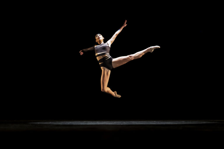 Girl performing contemporary dance on dark stage.