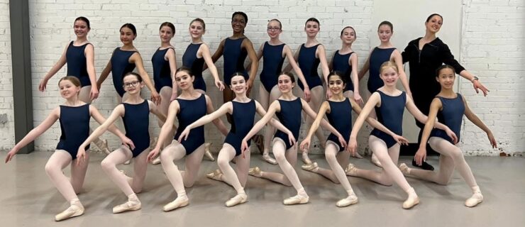 Sandre poses with her students who stand in two lines, the top line standing while the bottom line kneels.