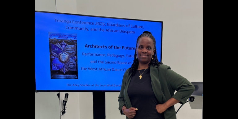 Dr. Andrea Markus standing in front of a presentation slide wearing a dress and blazer.