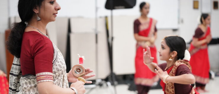 Sheela Ramanath in a white and red saree teaching in front of a classroom of Indian classical dancers.