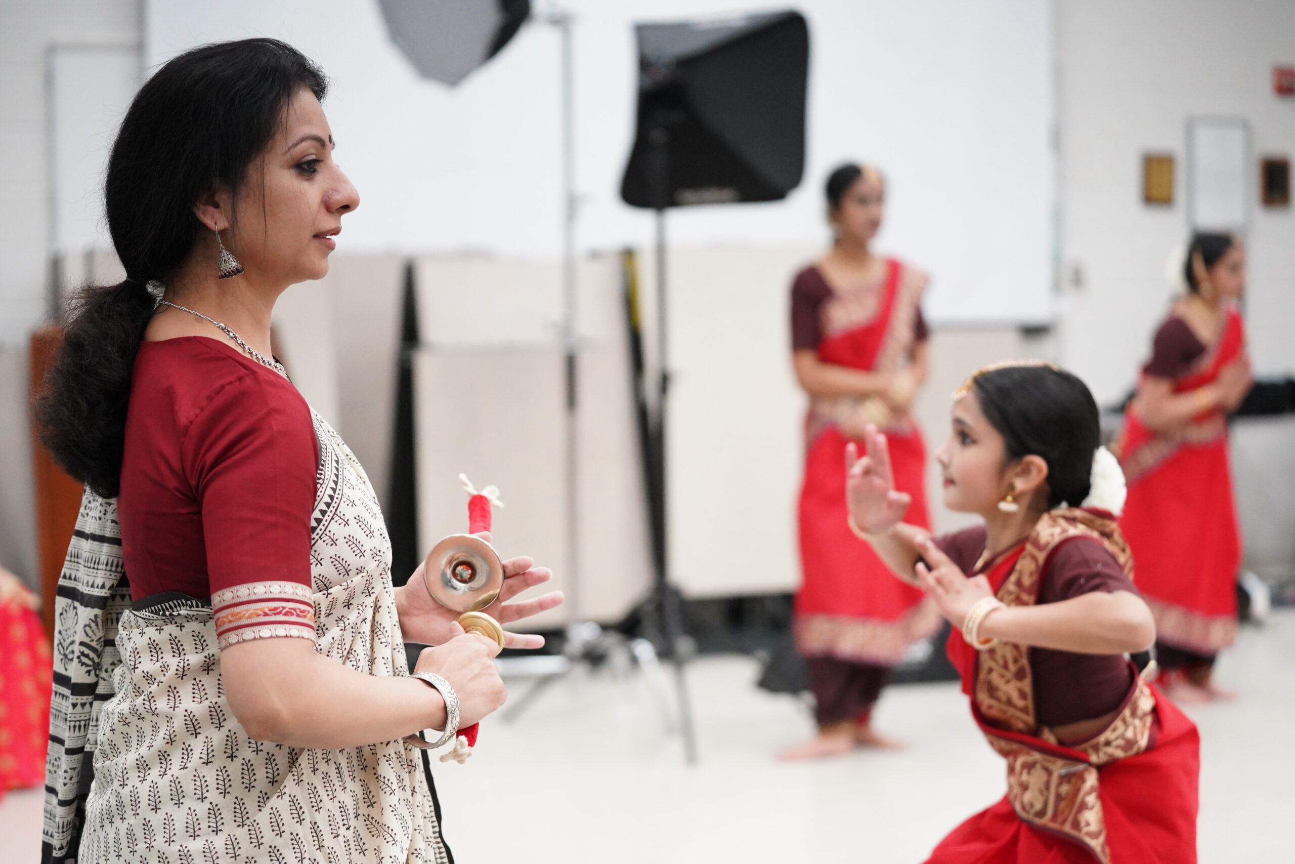 Sheela Ramanath in a white and red saree teaching in front of a classroom of Indian classical dancers.