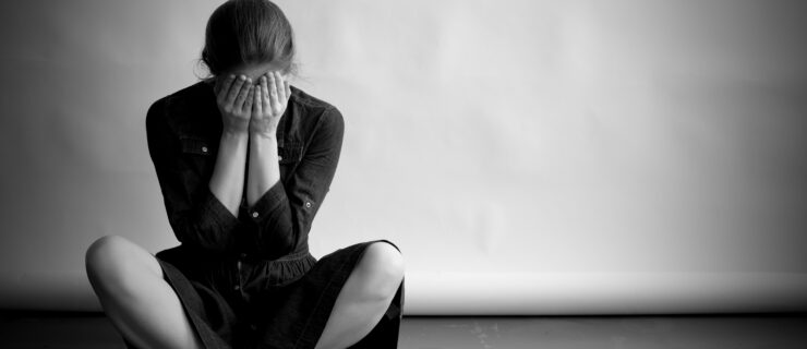 Depressed woman in monochrome sits with her face in the hands and crossed-legged on the floor.