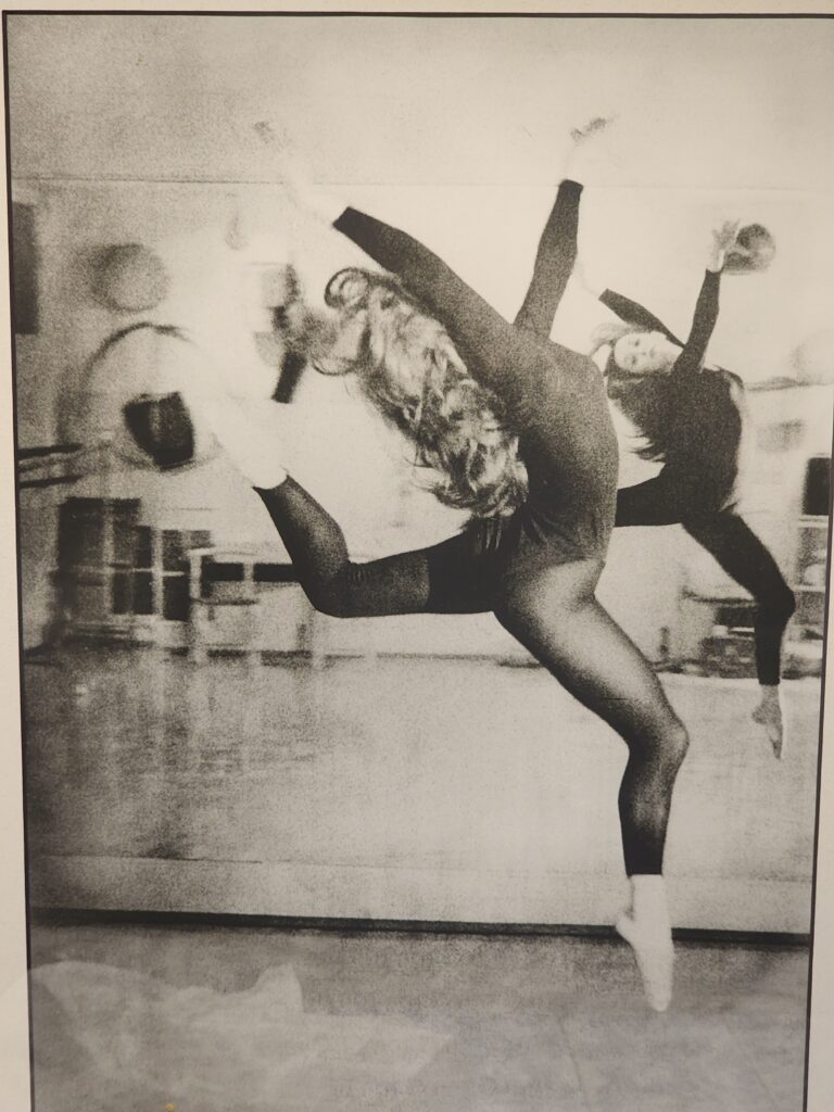 Black and white image of Kitty Lunn leaping in front of a dance mirror.