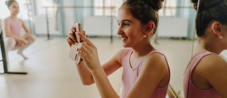 Young ballet student holding a phone to film/photograph in the studio.