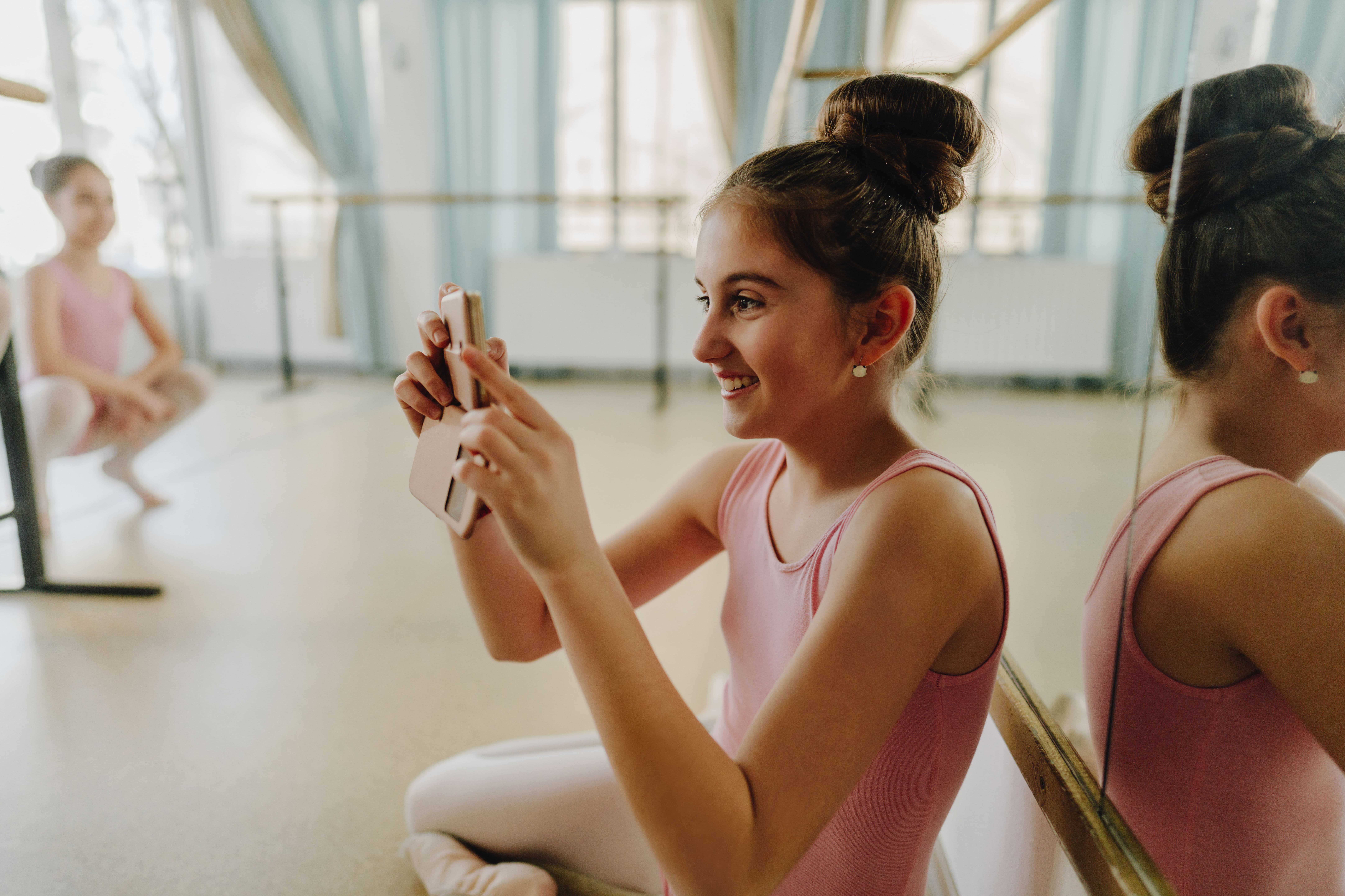 Young ballet student holding a cellphone to film in class.